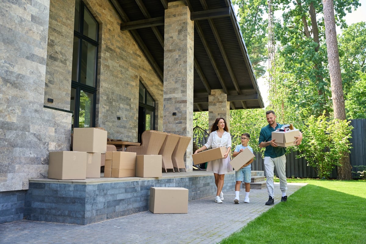 Parents and son move boxes with things to a new house, they chat cheerfully