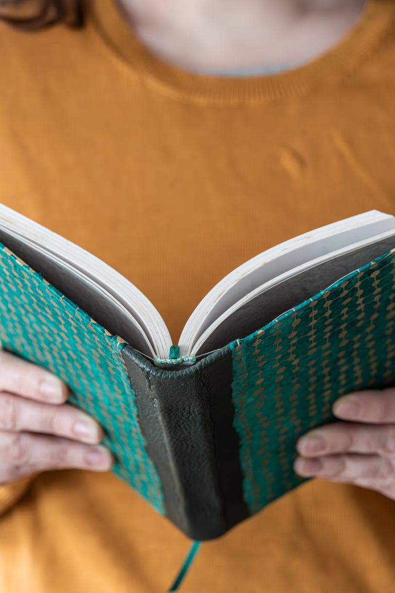 Woman holding an open book with a beautiful teal and gold cover, enjoying a moment of reading