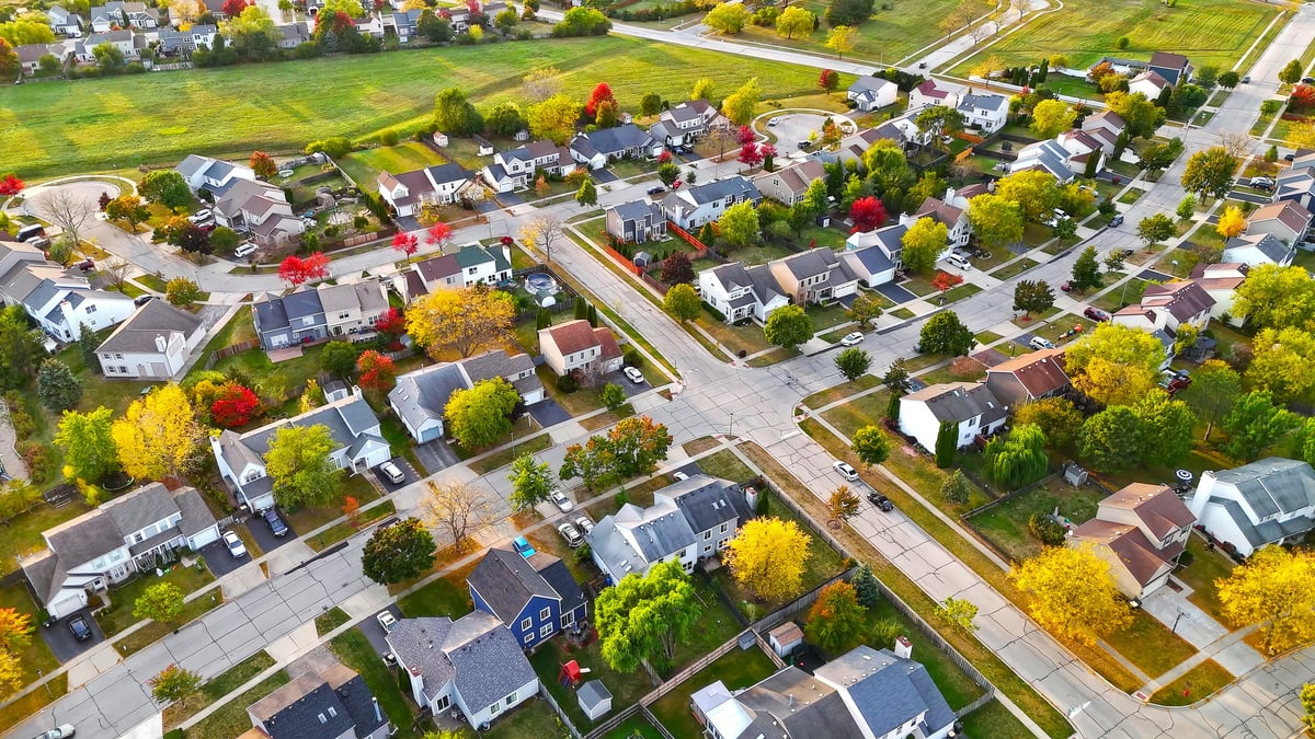 Aerial view of a suburban neighborhood in autumn with colorful trees, houses, and open green space