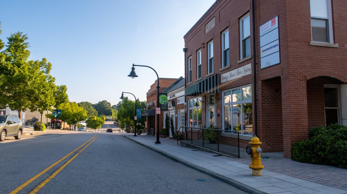 A quiet morning view of historic downtown Wake Forest, North Carolina, featuring classic brick storefronts, tree-lined sidewalks, and vintage street lamps under clear blue skies