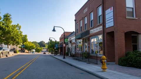 A quiet morning view of historic downtown Wake Forest, North Carolina, featuring classic brick storefronts, tree-lined sidewalks, and vintage street lamps under clear blue skies