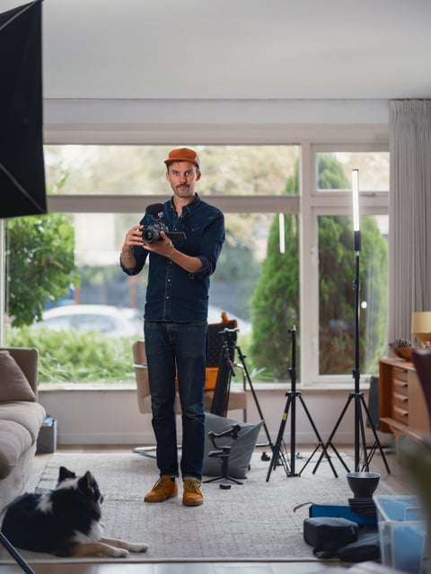 Man in denim holding camera to eye level preparing to shoot in bright residential studio