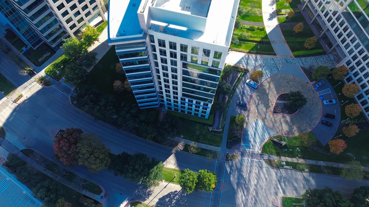 Tech hub Plano office framed by glass facade, autumn-colored trees, landscaped median street, sidewalk, blending seasonal natural elements with modern commercial architecture, infrastructure, TX. USA