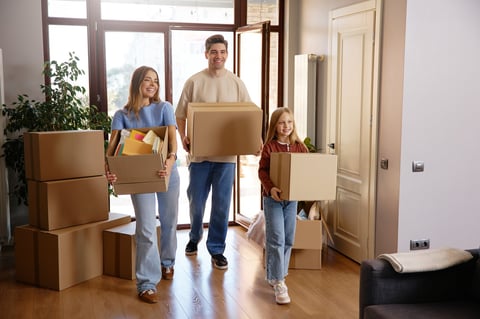 Cheerful family of three with cardboard boxes during house moving. Bright interior, teamwork, and joyful expressions. Concept of relocation, fresh start and family support.
