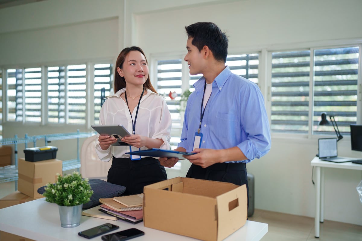 Young adult Asian business people discuss relocation plans. They analyze documents using a tablet and clipboard in a bright modern office.