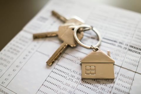 House keys on wooden table with bank account book in background. Concept of home ownership, financial planning for real estate investment, property mortgage, and saving for dream house.