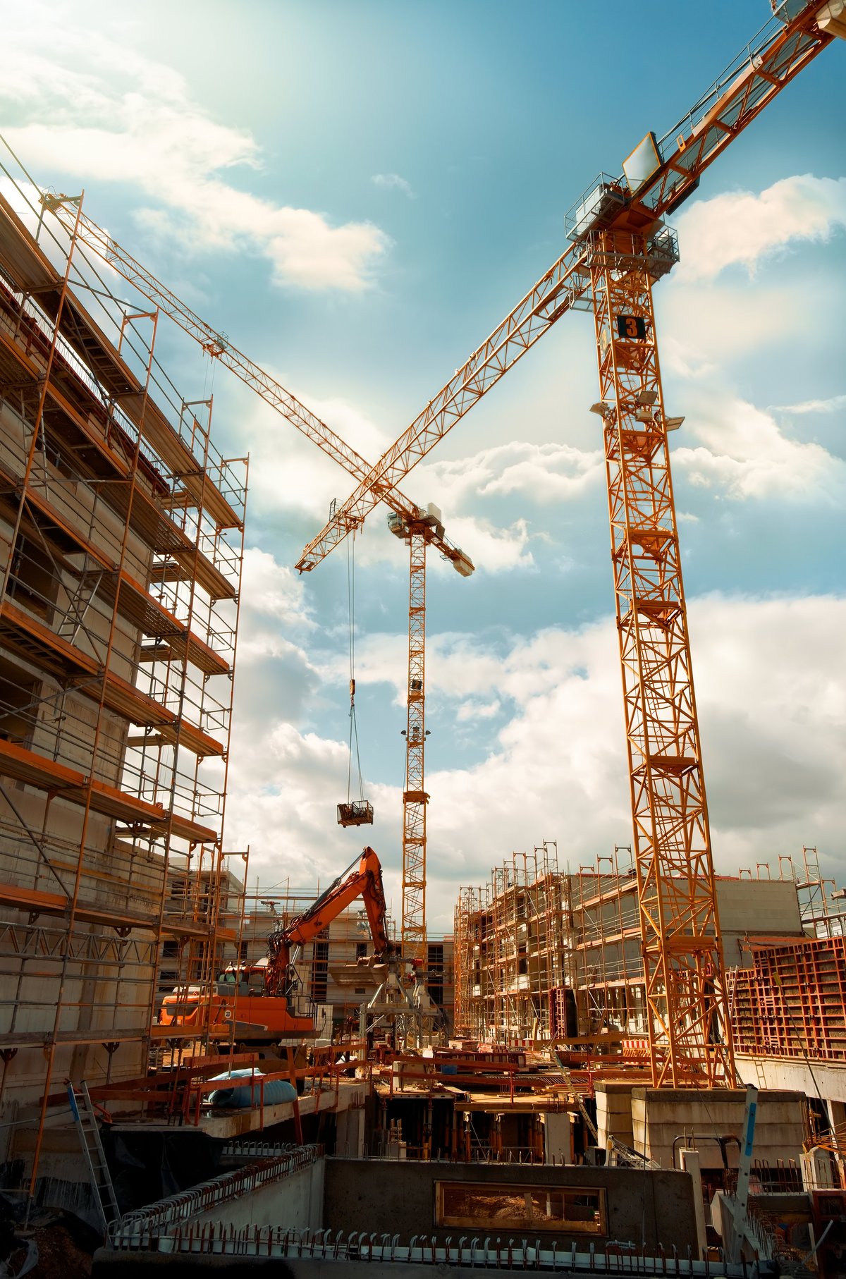 Construction site with yellow cranes looming into the blue sky with dramatic clouds. Wide angle tilted up view.