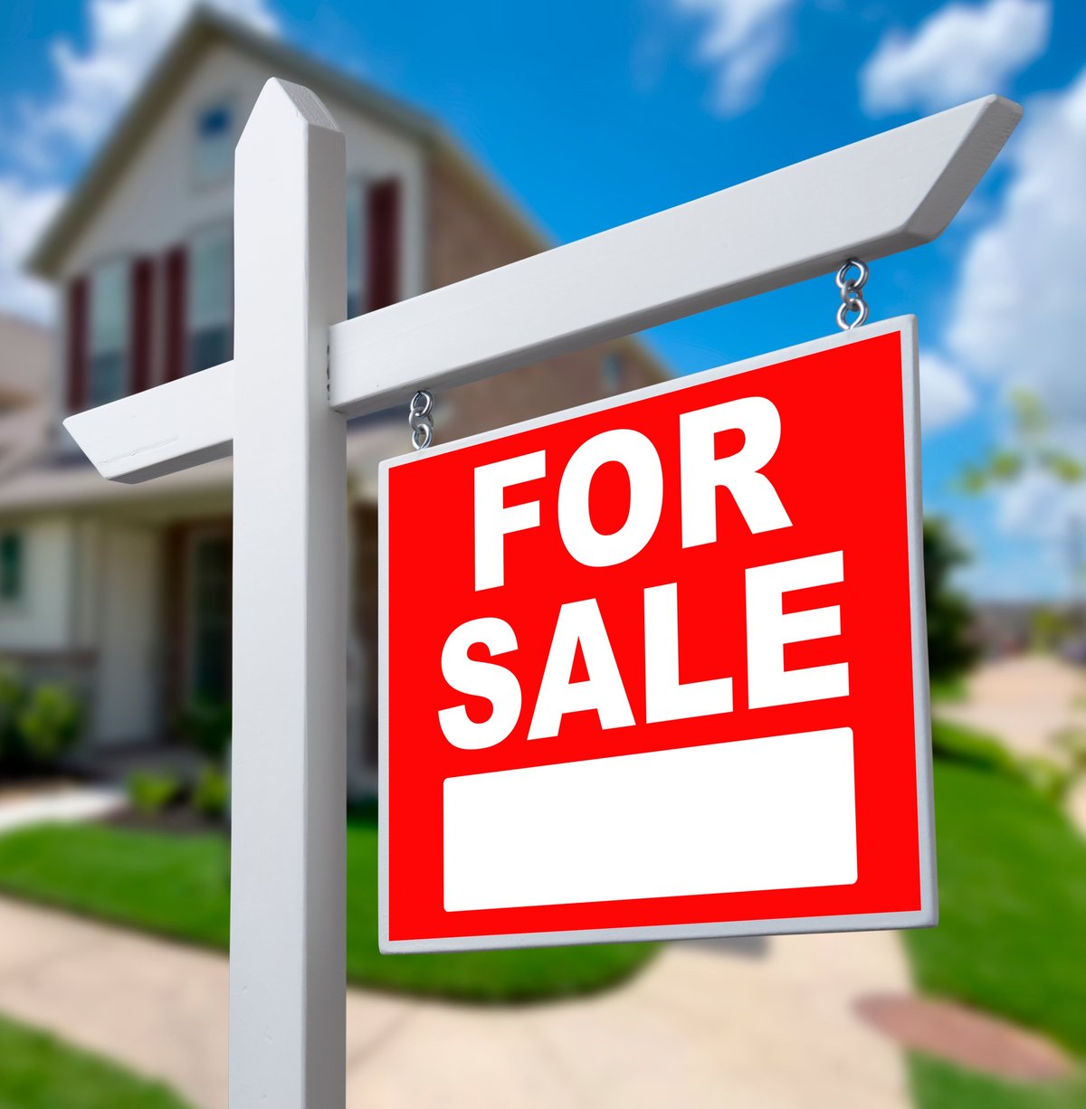A bright red sign says For Sale stands outside a house. The house is located in a neighborhood with clear sky.