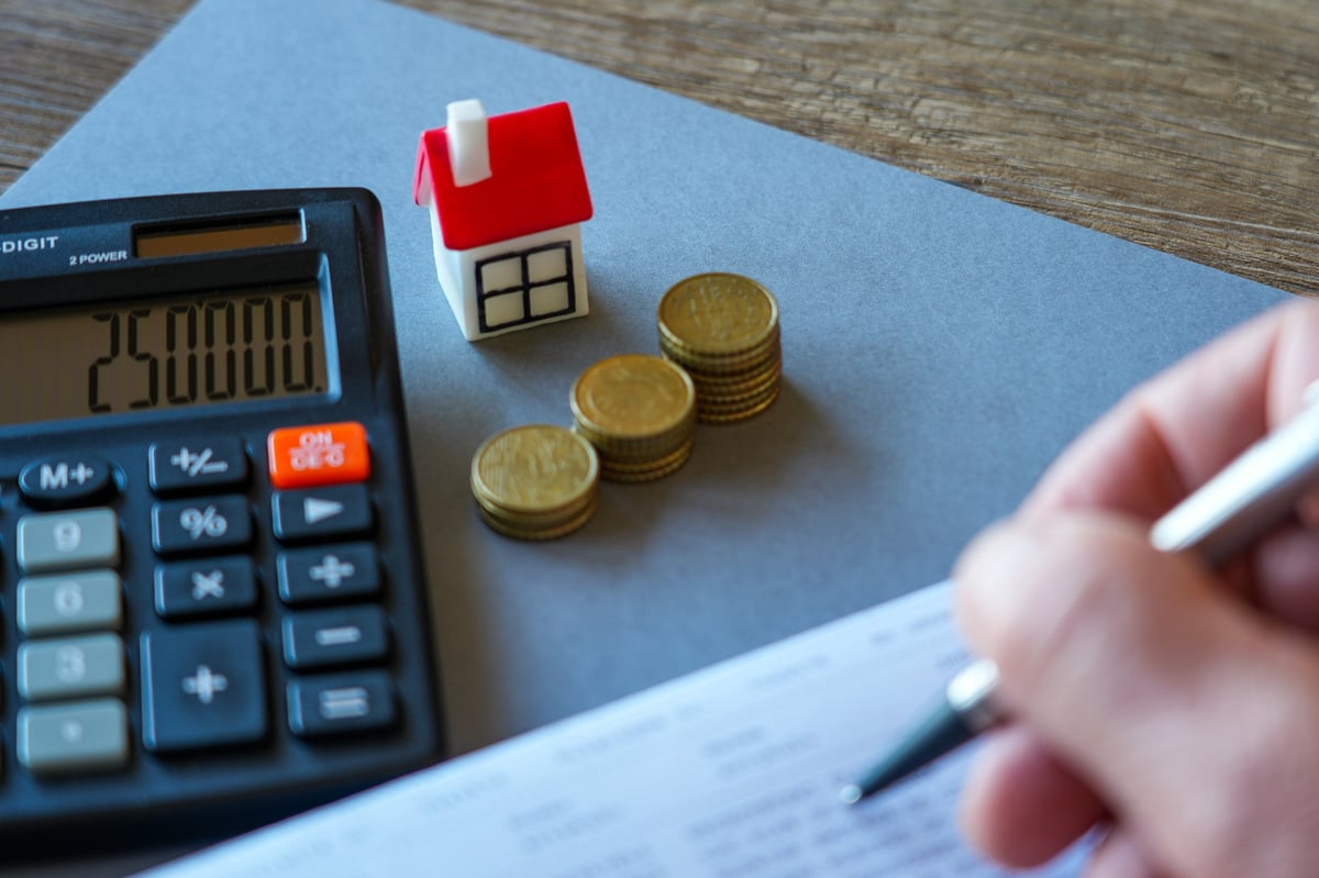 Calculator, miniature house, coin stacks and financial paperwork illustrate home budgeting, mortgage planning, savings and real estate investment