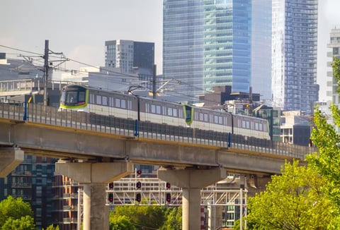 Montreal, Quebec, Canada. July 27, 2026. Side view of automated REM light rail train traveling on elevated track before downtown skyscrapers.
