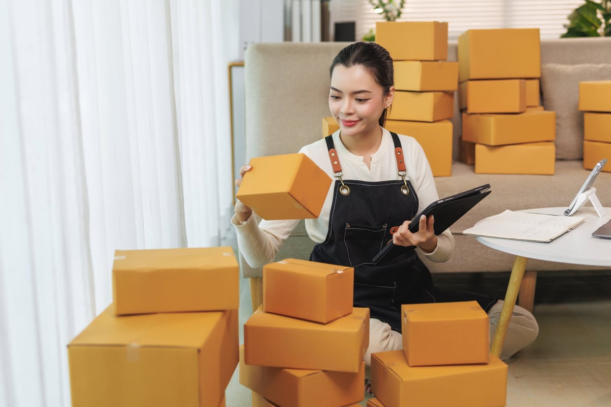 Young adult woman checking order details and packing products for delivery in her online store fulfillment process