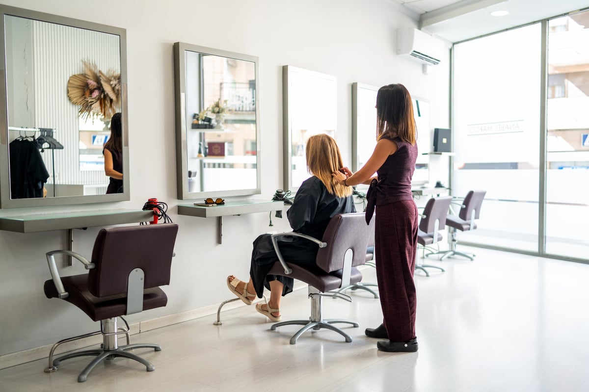 Female professional styling client's hair, offering beauty services in a bright, contemporary salon