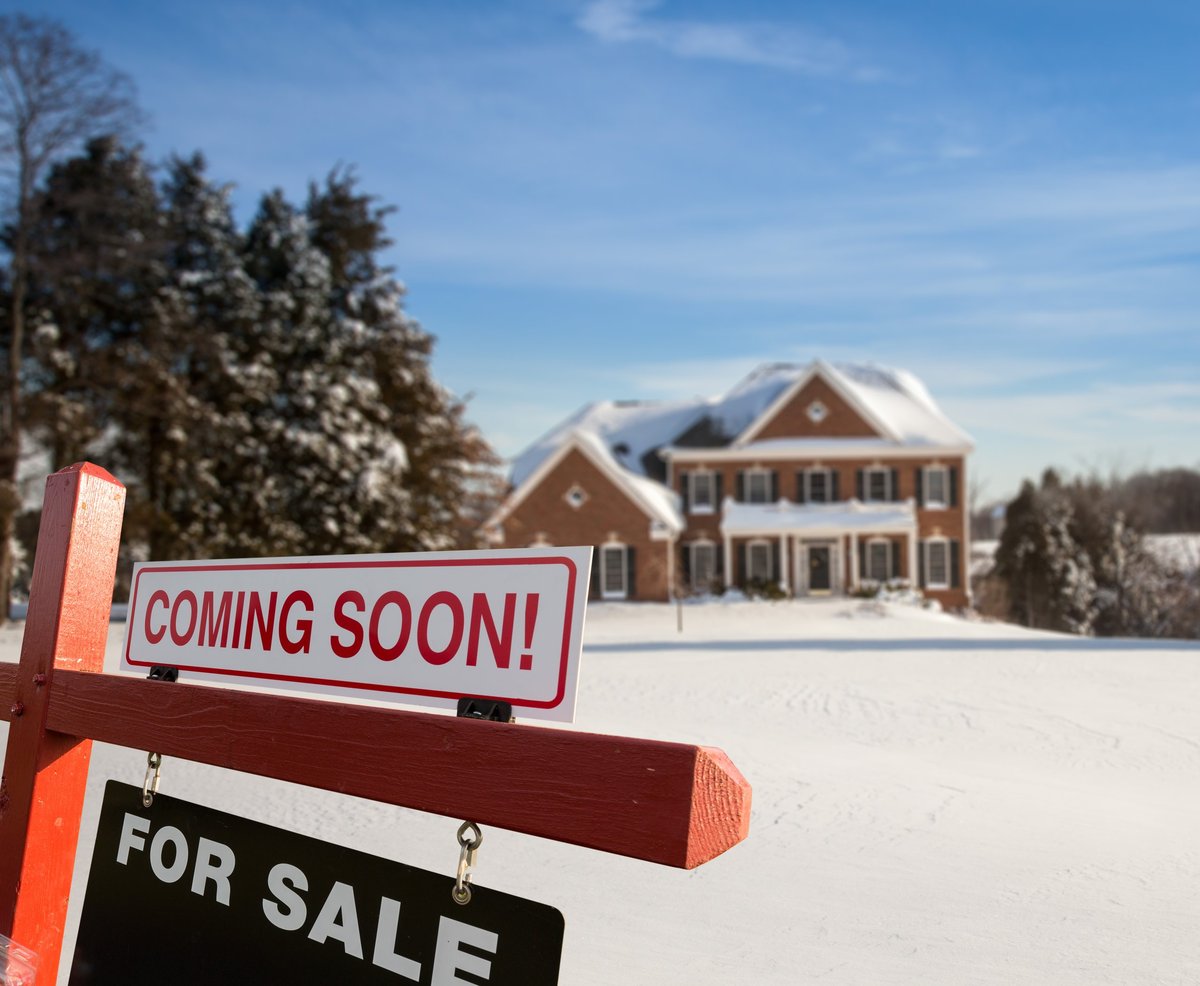 For Sale and Coming Soon Real Estate Agent sign in front of large brick single family house in expansive snow cover yard in mid winter