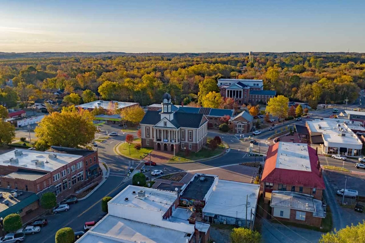 Aerial view of a town center with a white church building, surrounding trees with fall foliage, and various commercial buildings and streets