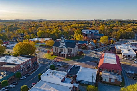 Aerial view of a town center with a white church building, surrounding trees with fall foliage, and various commercial buildings and streets