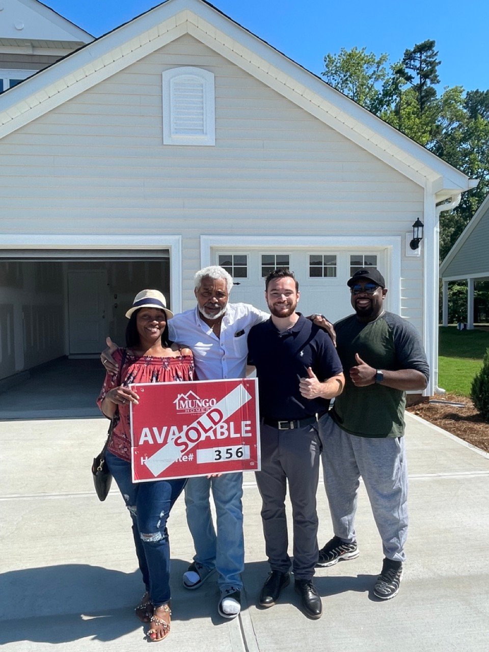 Four people standing in front of a white garage holding a red available property sign