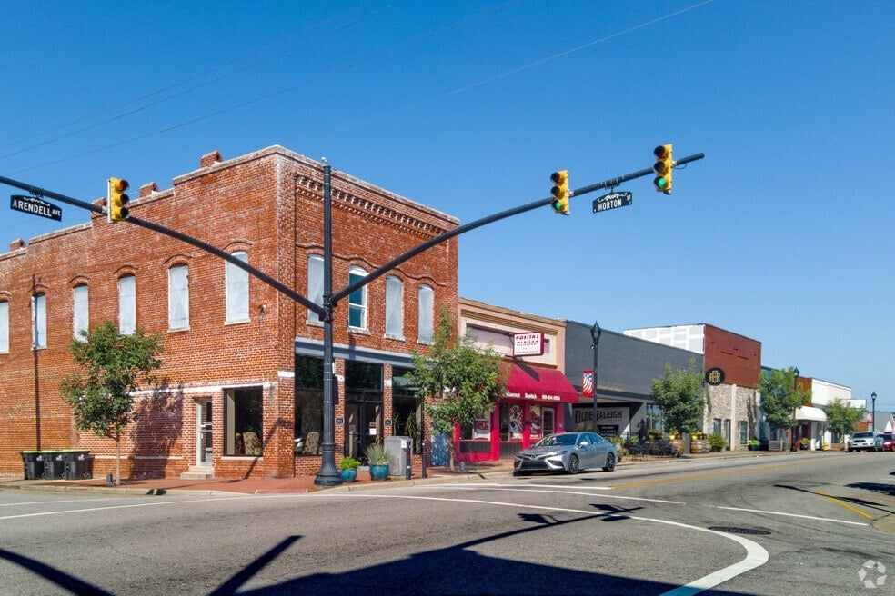 Historic brick building at a downtown street corner with traffic lights, storefronts, and blue sky