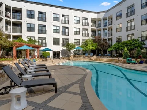 Modern apartment complex courtyard with outdoor swimming pool, lounge chairs, and white residential buildings surrounding the area