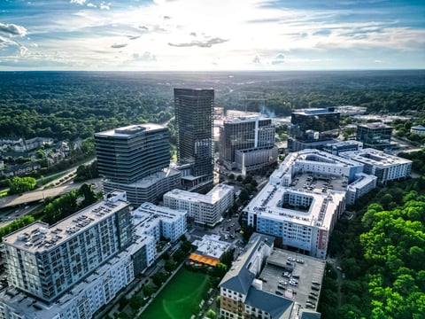 Aerial view of a downtown urban district with modern office and residential buildings surrounded by green forests and blue sky