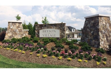 Bryson Village entrance sign with stone pillars, landscaping, and residential home in background